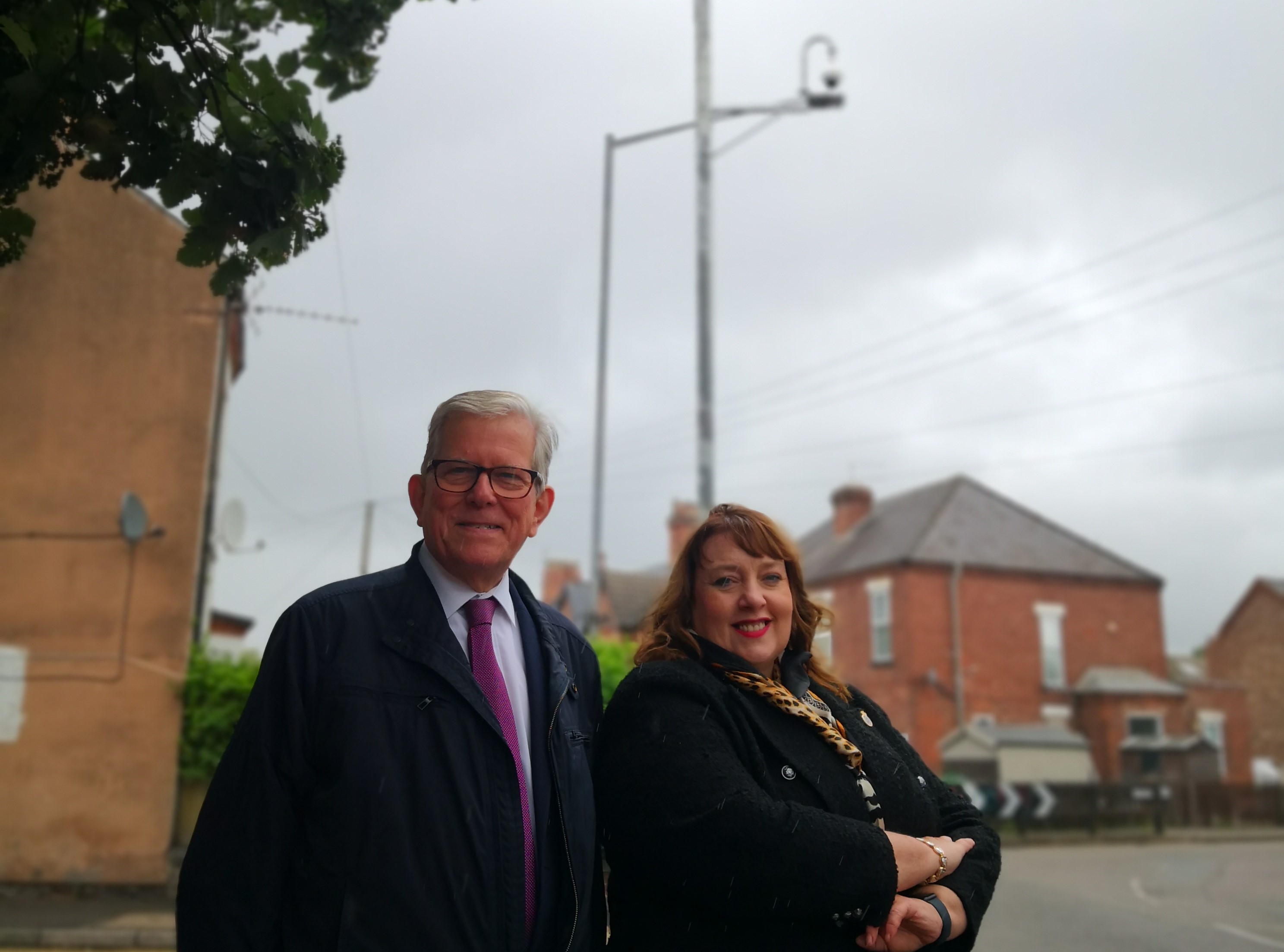 from left to right – Leader of Gedling Borough Council, Councillor John Clarke MBE with Nottinghamshire Police and Crime Commissioner Caroline Henry at the new CCTV Camera on the corner of Balmoral Road, Colwick. The camera is at the top of a large pole and is in the background slightly out of focus.